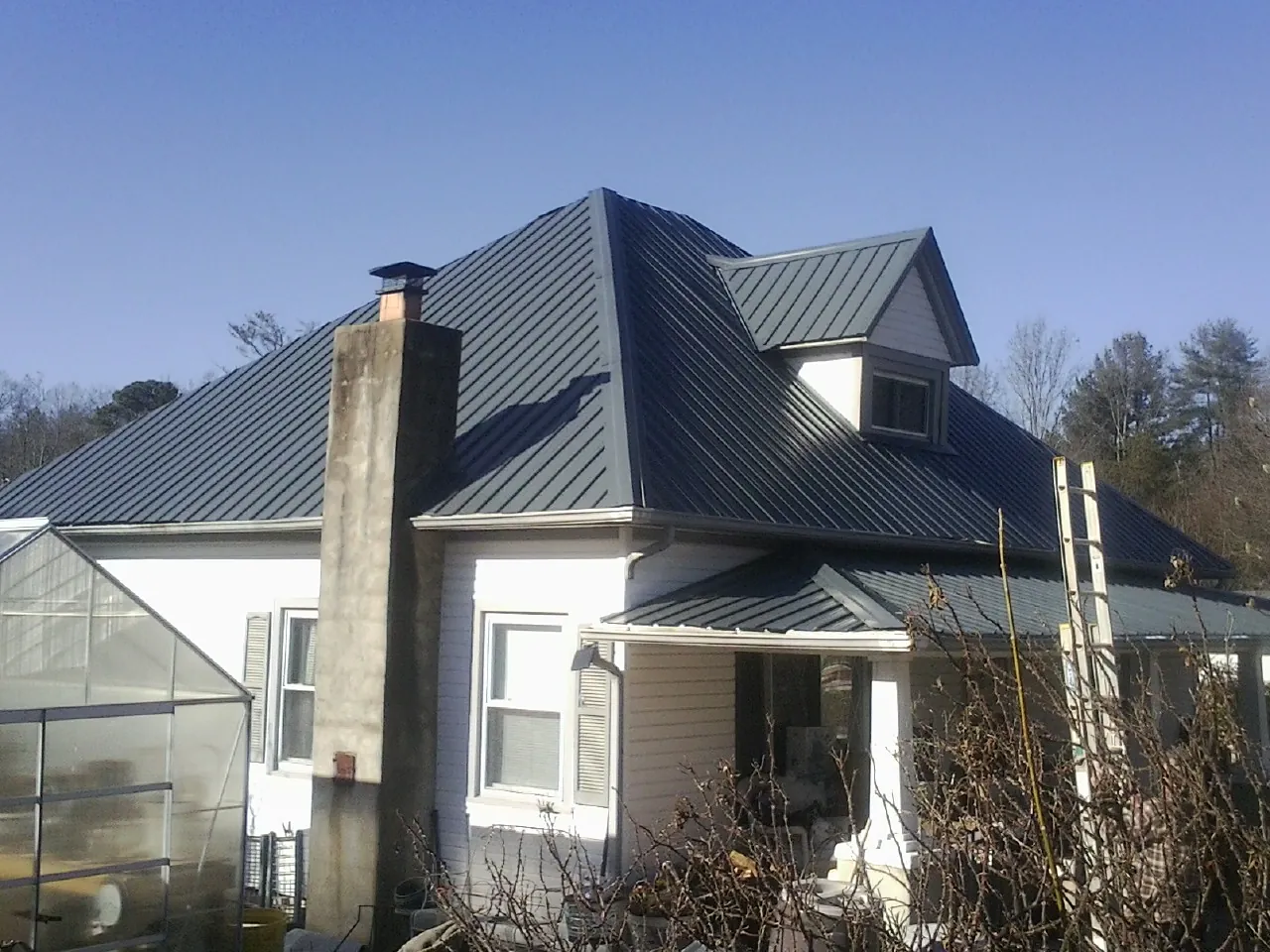Dark blue standing seam metal roof on a white farmhouse with dormer — Slate & Tile Roof Repair by Roofing Brothers in Jackson