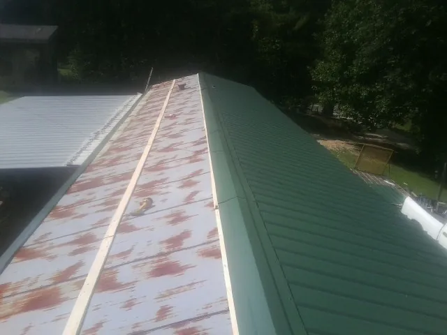 Old rusted panels beside newly installed green metal roofing — Wind Damage Roof Repair by Roofing Brothers in Jackson